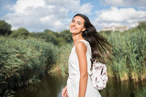 Belo retrato sorridente jovem com mochila no fundo do lago, no fundo da natureza. Caminhando no parque. Viajar. Férias — Fotografia de Stock