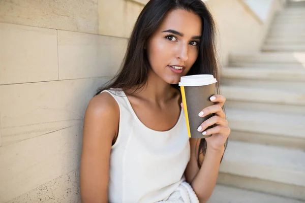 Belo retrato close-up de jovem mulher morena atraente com uma xícara de café ou chá, sentado nos degraus do parque. Olhando para a câmera — Fotografia de Stock
