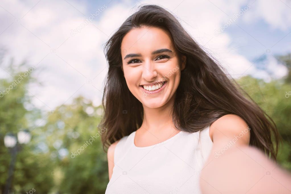 Beautiful self portrait of young brunette smiling woman on nature and sky background in the park. Travel. Selfie. Instagram