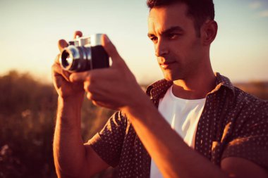 Vintage fotoğraf makinesi alan arka plan ve Günbatımı ile genç güzel adam yakışıklı portresi. Sonbahar, yaz, ruh hali. Fotoğraf