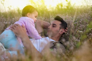Yakışıklı mutlu genç baba oynamak ve onun güzel mutlu yürümeye başlayan çocuk kız çim ile gülüyor. Onun bebek kız çayır on yürüyüş ile mutlu baba.