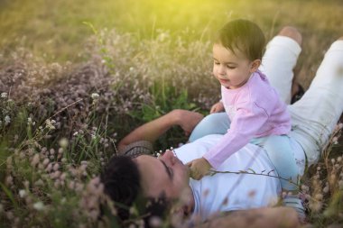 Mutlu genç baba oynamak ve onun güzel mutlu yürümeye başlayan çocuk kız çim ile gülüyor. Onun bebek kız çayır on yürüyüş ile mutlu baba.