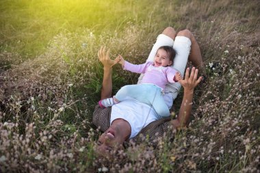 Şirin mutlu yürümeye başlayan çocuk kızının oynarken ve çim üzerinde gülüyor yüze oturan babası yukarıda görüntüleyin. Mutlu baba ile bebek sevgilisini bir güneşli bir gün veya gece. Çayır üzerinde yürüme aile.