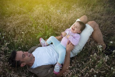 Şirin mutlu yürümeye başlayan çocuk kızının oynarken ve çim üzerinde gülüyor yüze oturan genç baba. Mutlu baba ile bebek sevgilisini bir güneşli bir gün veya gece. Çayır üzerinde yürüme aile.
