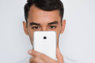 Genç adam cep telefonuyla gri arka plan üzerinde güzel yakın çekim portre. Akıllı telefonda konuşan işadamı. Kırpılan yüz.