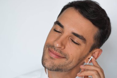 Yakın çekim yakışıklı beyaz genç adam onun favori müzik keyfi portresi. Gri bir arka plana dayanır Kulaklığımda mutlu şık gülümseyen adam. Kapalı gözlerle rahatlama müzik.