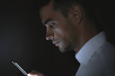 Yakın çekim yakışıklı delikanlı koyu arka plan üzerinde elinde akıllı telefon kullanarak portresi