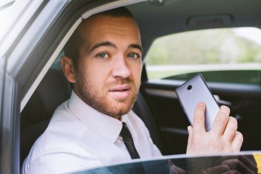 Açık araba pencereden dışarı bakarak ve araba arka koltukta oturan akıllı telefon arama yakışıklı beyaz ciddi işadamı yatay portresi. Teknoloji ve iş kavramı.