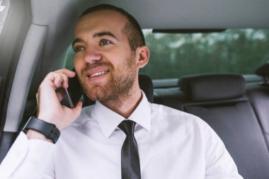 Yatay akıllı telefon ve araba arka koltukta oturan ve araba pencereden dışarı bakarak: çağrı yakışıklı beyaz gülümseyen işadamı portresi kapatın. Teknoloji ve iş kavramı.