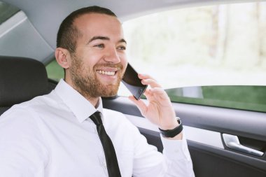 Başarı hakkında akıllı telefon arama ve araba arka koltukta oturan mutlu bir yakışıklı işadamı portresi. Teknoloji ve iş kavramı.