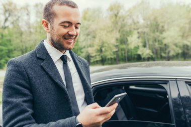 Cep telefonunuzda e-posta denetimi ile araba, bir palto giyiyor şık ciddi yakışıklı genç beyaz kişi. Yaşam tarzı, insan ve modern teknoloji.