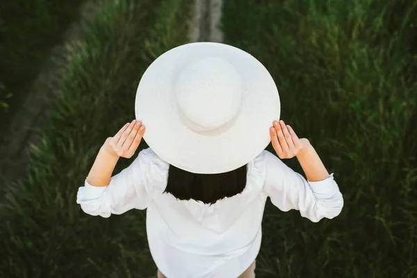 Sfondo fantastico. Ritratto di bella e adorabile, affascinante vista posteriore di giovane bella donna bruna con le mani su un cappello, su sfondo campo verde . — Foto Stock