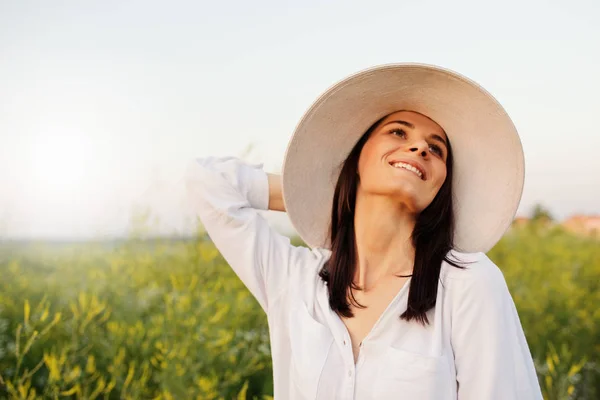 Портрет романтичной красивой и привлекательной молодой женщины в шляпе и белой рубашке, мечтающей, смотрящей в небо, на природу, на полевой фон. Красота — стоковое фото