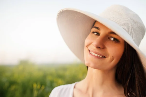 Close up retrato de uma mulher bonita atraente romântico com um chapéu e camisa branca, sorrindo e olhando para a câmera na natureza, fundo de campo. Beleza — Fotografia de Stock