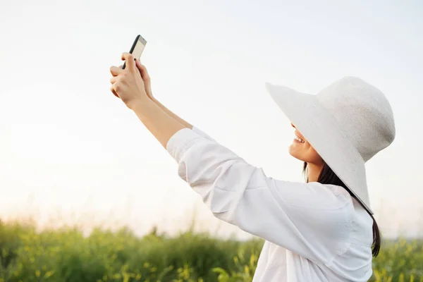 Amazing attractive romantic young woman with hat and white shirt smiling and taking selfie on the phone, on nature, field background. Instagram — Stock Photo, Image