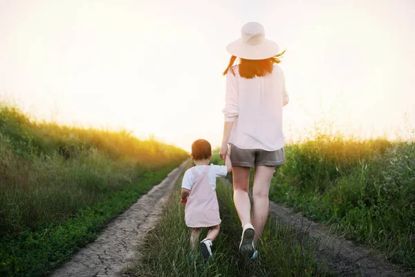 Encantadora, adorável e incrível vista de caminhar de uma mãe bonita e bela filhinha em um campo de caminho. Maternidade e infância. Pôr do sol ou nascer do sol . — Fotografia de Stock