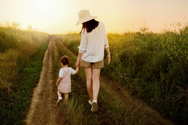 Удивительный, очаровательный, очаровательный вид на красивую мать в шляпе и маленькую красивую дочь, идущую по тропе поля. Закат или восход солнца. Материнство и детство — стоковое фото