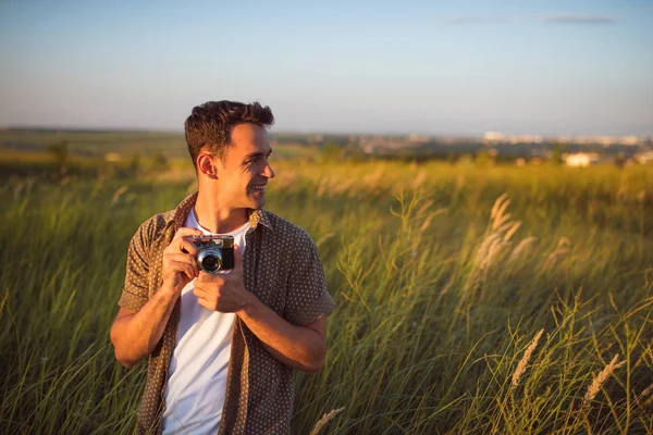 Bonito jovem viajante com câmera vintage, em um fundo prado verde. Humor de viagem. Fotografia. Relaxamento em um campo e por do sol. Explore a natureza . — Fotografia de Stock