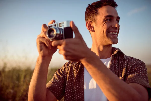 Belo retrato de belo sorriso jovem com câmera vintage, em um fundo de prado. Humor de viagem. Fotografia. Relaxamento em um campo e por do sol. Explore a natureza . — Fotografia de Stock