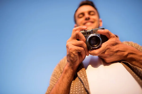Alulnézet mosolygó csinos, fiatal férfi vintage kamerával, hogy a képet a háttérben ég. Ősszel. Nyári. Hangulat háttér. Fotózás. — Stock Fotó