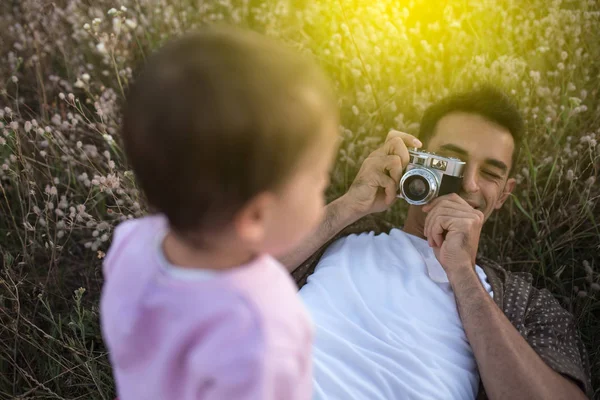 Yukarıdan bir şirin mutlu yürümeye başlayan çocuk kızının oynarken ve çim üzerinde gülüyor yalan baba görüntüleyin. Mutlu baba onun bebek kız fotoğraf ile fotoğraf makinesi ile. Çayır üzerinde yürüme aile.