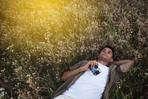 Amazing view from above of handsome young man with vintage camera, lying on meadow background. Travel mood. Photography. Relaxation on a field. — Stock Photo, Image
