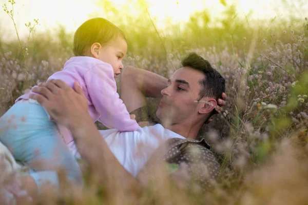 Yakışıklı mutlu genç baba oynamak ve onun güzel mutlu yürümeye başlayan çocuk kız çim ile gülüyor. Onun bebek kız çayır on yürüyüş ile mutlu baba.