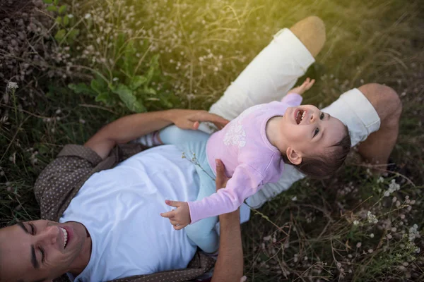 Widok z góry szczęśliwy młody ojciec gra i się śmiać z jego dziewczyna ładna szczęśliwego malucha na trawie. Szczęśliwy tata z jego dziewczynka chodzenie na łące. — Zdjęcie stockowe