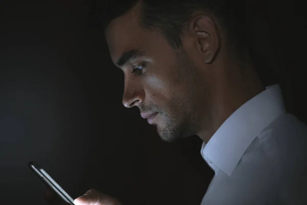 Close-up portrait of young handsome man using smart phone in hand on dark background — Stock Photo, Image