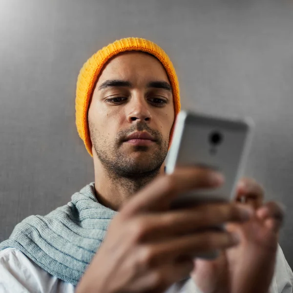 Bottom view. Close-up portrait of young man with a gadget, telephone, wearing orange hat and gray scarf. Reading, typing or playing the game. — Stock Photo, Image