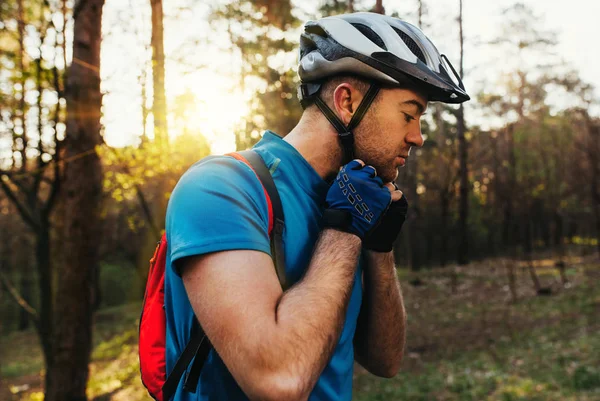 Retrato atraente de belo ciclista barbudo usando capacete protetor antes da corrida, em pé na floresta contra o fundo das árvores verdes. Jovem cavaleiro usando mochila vermelha.Viajar. Estilo de vida desportivo . — Fotografia de Stock