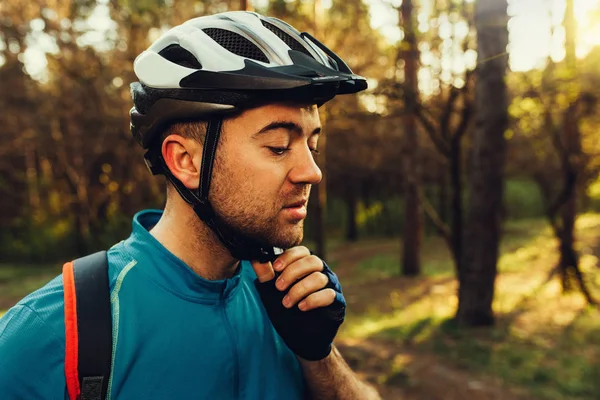 Close up portrait Young serious bearded rider wearing blue t-shirt, closing his protective helmet outdoors and looking down, thinking about cycling. Travel concept. Sport lifestyle. — Stock Photo, Image