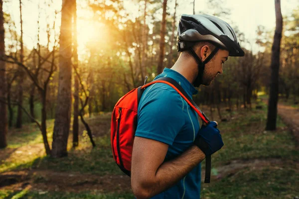 Retrato no perfil de belo jovem ciclista barbudo vestindo capacete protetor, camiseta azul e mochila vermelha, olhando para baixo, pensando em rota e ciclismo. Conceito de viagem. Estilo de vida desportivo . — Fotografia de Stock