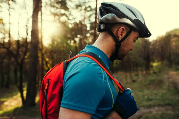 Beautiful close up shot of handsome young bearded man cyclist wearing protective helmet, blue t-shirt and red backpack, looking down, thinking about route and cycling. Travel concept. Sport lifestyle.