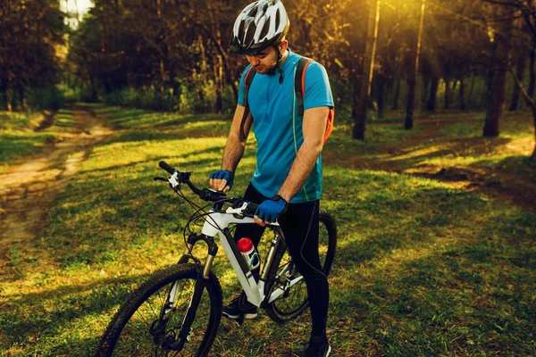 Beautiful shot outdoor of professional rider wearing cycling clothing and helmet during workout in park, making settings on control panel on bicycle before ride in mountain. Travel lifestyle. — Stock Photo, Image