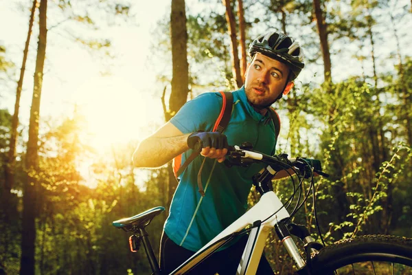 Stilig allvarliga manliga biker bär blå sport kläder, hjälm och handskar, har Självsäker och självbestämt blick på skogen solnedgång eller soluppgång. Resor, sport, extrema koncept. — Stockfoto