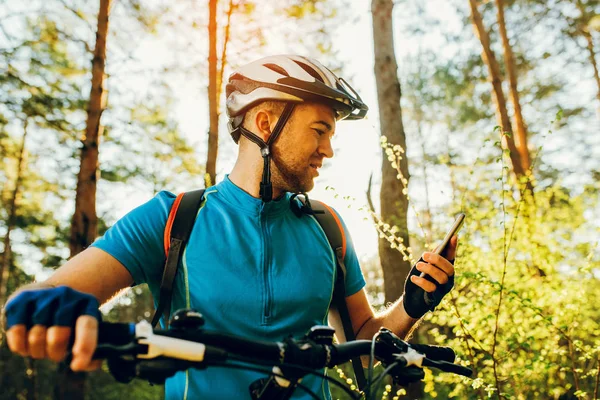 Vista inferior e lateral do ciclista de bicicleta usando o navegador no smartphone, explore o mapa e pesquise coordenadas GPS enquanto pedala nas montanhas. Viagens, esportes, estilo de vida ativo e tecnologia moderna . — Fotografia de Stock