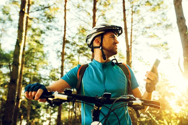 Dołu widok zewnątrz strzał rowerzysta na rower za pomocą nawigatora na inteligentny telefon, odkrywaj mapę i Szukaj współrzędne Gps podczas jazdy na rowerze w górach. Podróże, Sport, aktywny tryb życia i nowoczesna technologia. — Zdjęcie stockowe