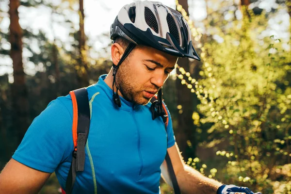 Outdoor shot of handsome young professional mountain biker in helmet and blue cycling t-shirt, standing outdoors in woods, getting ready for cycling contest. — Stock Photo, Image