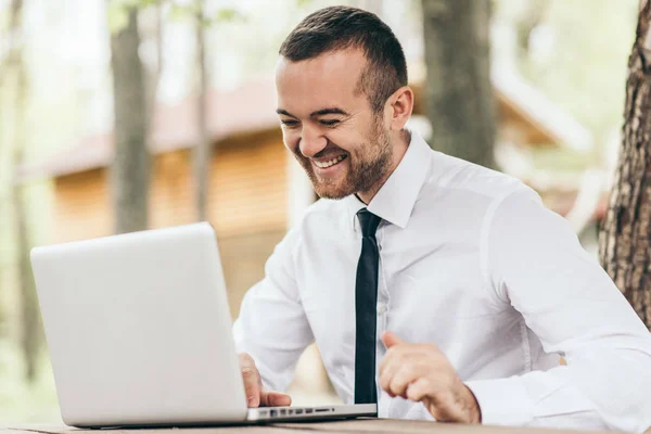 Veselá pohledný muž v bílé košili u stolu pomocí moderních technologií s potěšením upřímným úsměvem zatímco internetové konverzace. Lidé, kariéru, emoce, technologický koncept. — Stock fotografie