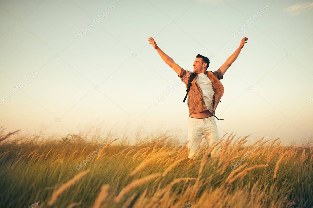 Handsome happy caucasian man with a backpack on his shoulders jump on a meadow, time to go traveling. Tourism concept. Travel adventure of active sport man.