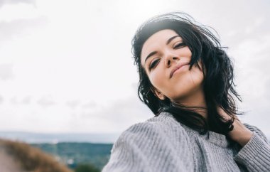 Kazak olmanın oynak ve kaygısız poz güneş ışığı gökyüzü ve arka plan üzerinde giyen güzel romantik esmer kadın yatay portresi. Seyahat, insanlar ve yaşam tarzı kavramı. Kapak fikir ruh hali.