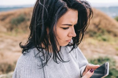 Ciddi Kafkas kadın manifatura alt görünümünü cep telefonu, akıllı telefon, dışarıda rüzgarlı saçlarıyla poz sosyal yaşam için kablosuz bağlantı kullanarak. İnsanlar, seyahat ve yaşam tarzı kavramı.