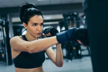 Güçlü çekici esmer kadın kickboxing eldivenli bir çanta içinde jimnastik salonu iş Delme yan görünüm. Spor, fitness, yaşam tarzı ve insanlar kavramı.