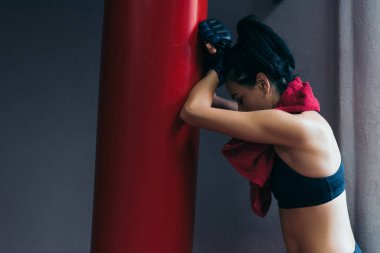 Kickboks eldivenler spor salonunda yan görünüm yorgun çekici esmer kadın kırmızı havlu ile boyun rahatlatıcı ve dinlenirken yumruk çanta üzerinde. Spor, fitness, yaşam tarzı ve insanlar kavramı.