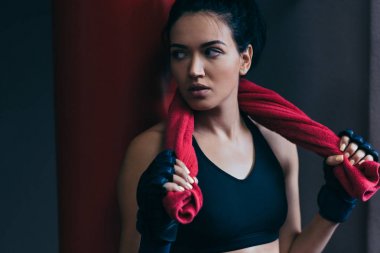 Sonra egzersiz ile karşı yumruk torbası, boynunda kırmızı havlu ile sportif çekici esmer kadın kickboxing eldivenler salonunda kırpılmış portresi. Spor, fitness, yaşam tarzı, insanlar kavramı.
