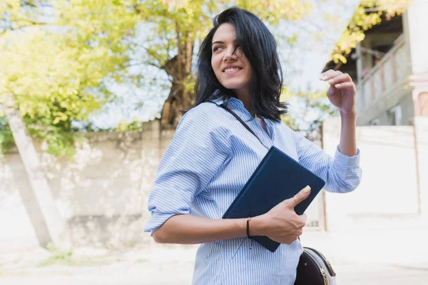 Mulher empresária morena alegre usando notebook para planejar o tempo para novos projetos ao ar livre. Jovem estudante inteligente vestindo camisa azul na rua. Negócios, pessoas, conceito de estilo de vida . — Fotografia de Stock