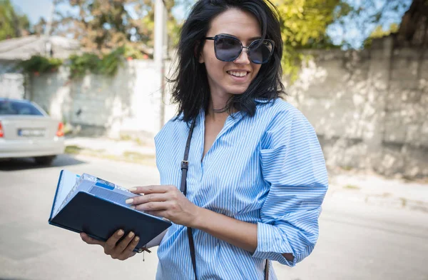 Pessoas, negócios, conceito de trabalho. Sorrindo alegre morena empresária gerente feminina usando bloco de notas para planejar o tempo para novos projetos ao ar livre. Jovem estudante inteligente usando óculos de sol na rua . — Fotografia de Stock