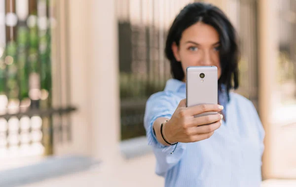 Horizontální portrét krásné mladé ženy dělá selfie na chytrý telefon, představuje na kameru při čekání kamarády v parku, bude příspěvek nové fotografie na své stránce sociální sítě. Kopírovat prostor. — Stock fotografie