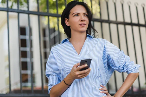 Yakın çekim portre seyir cep telefon uzakta ve bekleyen arkadaşıyla şehrin sokak üzerinde ciddi çekici kadın. Akıllı telefon tutarak ve kontrol genç esmer dalgın iş kadını. — Stok fotoğraf